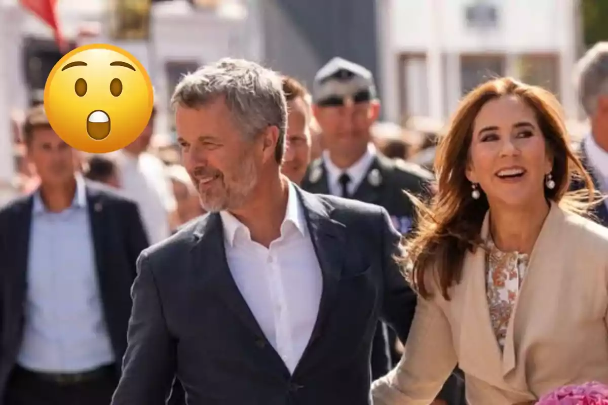 Federico y Mary de Dinamarca sonrientes caminan entre una multitud al aire libre mientras un emoji de cara sorprendida cubre a una persona en el fondo