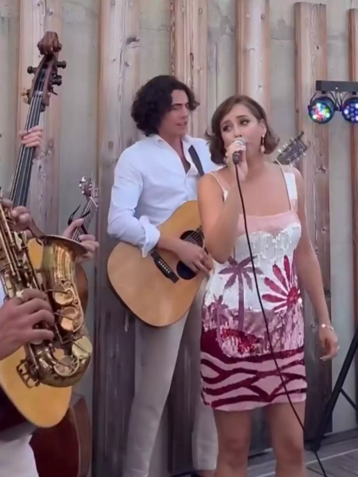 Grupo musical tocando al aire libre con una cantante al frente y músicos tocando guitarra, saxofón y contrabajo, todos vestidos de manera elegante Grupo musical tocando al aire libre con una cantante al frente y músicos tocando guitarra, saxofón y contrabajo, todos vestidos de manera elegante