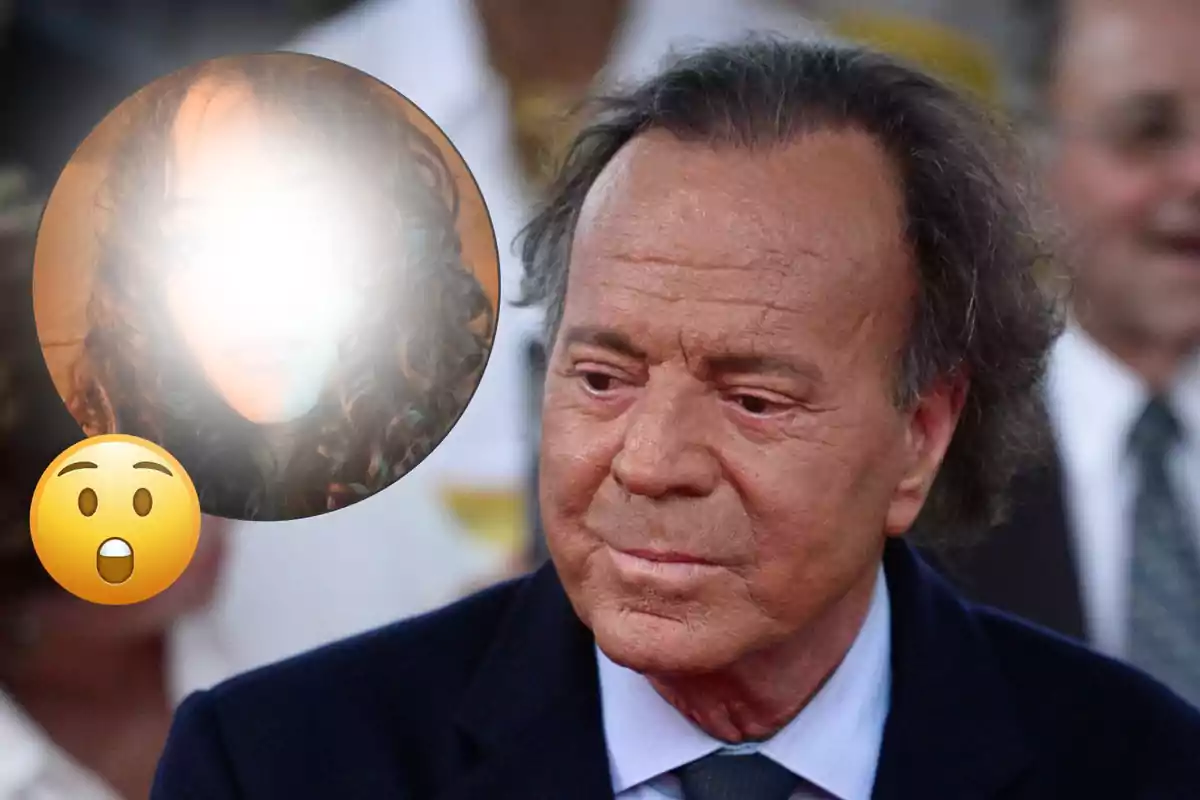 Julio Iglesias de cabello canoso y expresión seria en primer plano con un círculo que muestra el rostro de una persona desenfocada y un emoji de sorpresa superpuesto