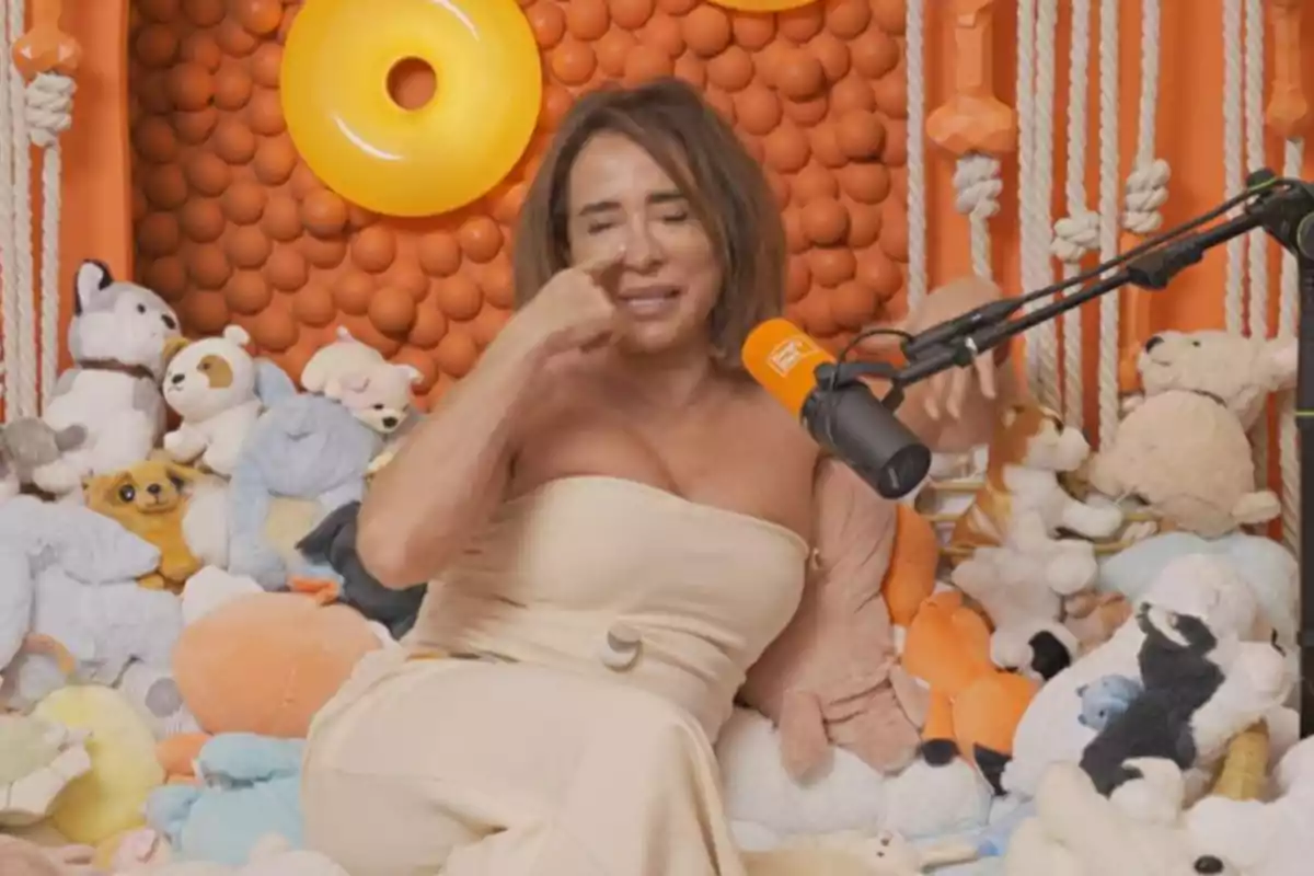 María Patiño sentada rodeada de peluches en un ambiente decorado con colores naranjas y micrófono frente a ella María Patiño sentada rodeada de peluches en un ambiente decorado con colores naranjas y micrófono frente a ella