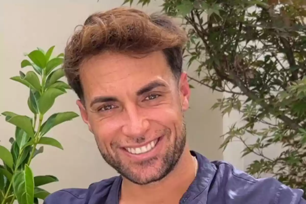 Home jove de cabell castany clar i barba curta somrient davant d’unes plantes Home jove de cabell castany clar i barba curta somrient davant d’unes plantes