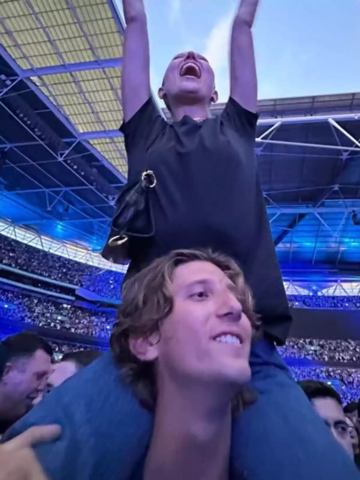 Una dona emocionada està asseguda sobre les espatlles d’un home en un estadi ple de gent durant un concert. Una dona emocionada està asseguda sobre les espatlles d’un home en un estadi ple de gent durant un concert.