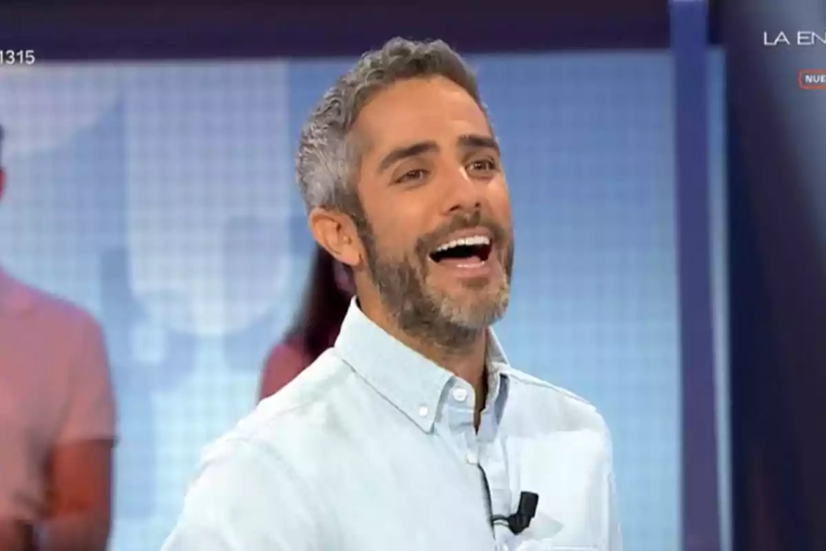 Home de cabells curts i barba canosa somrient en un plató de televisió amb camisa clara Home de cabells curts i barba canosa somrient en un plató de televisió amb camisa clara