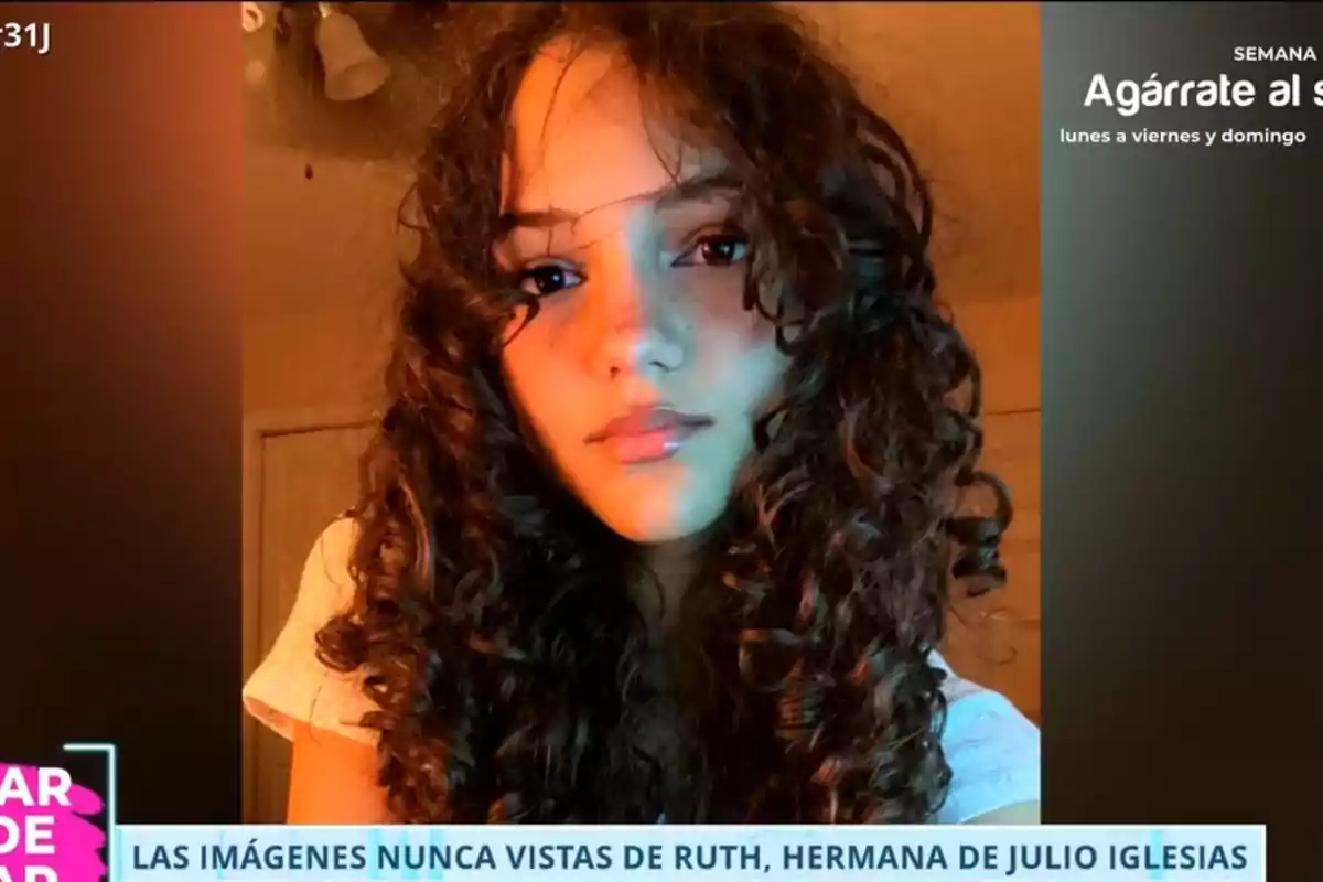 Ruth de cabello rizado y largo mirando a la cámara con expresión seria en una habitación iluminada con luz cálida, en la parte inferior hay un texto informativo de un programa de televisión. Ruth de cabello rizado y largo mirando a la cámara con expresión seria en una habitación iluminada con luz cálida, en la parte inferior hay un texto informativo de un programa de televisión.