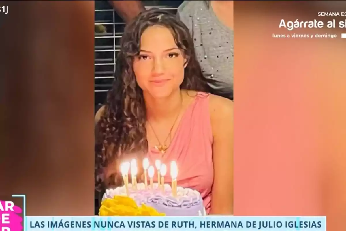 Ruth con cabello rizado y vestido rosa sonríe frente a un pastel de cumpleaños con velas encendidas Ruth con cabello rizado y vestido rosa sonríe frente a un pastel de cumpleaños con velas encendidas