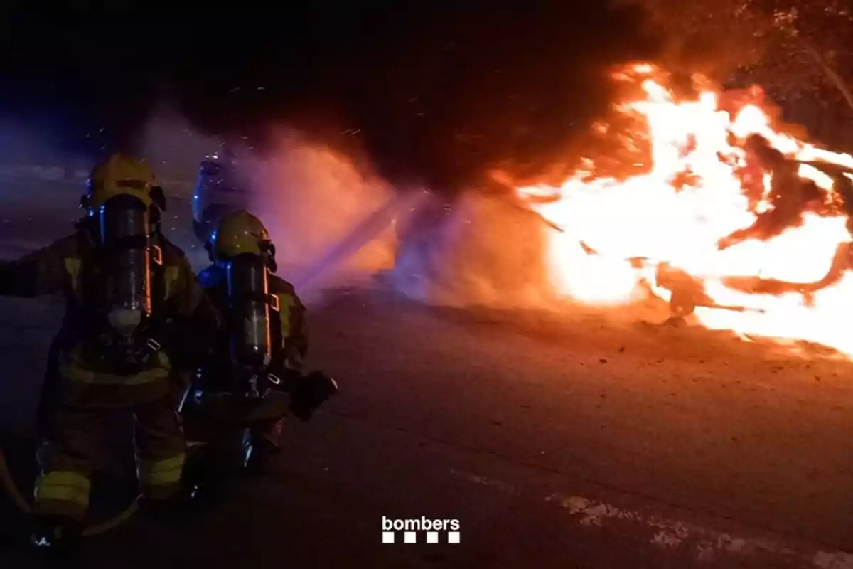 Dos bombers apaguen un incendi d’un vehicle al mig del carrer durant la nit