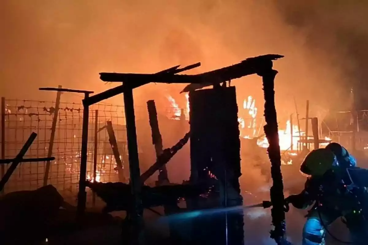 Un bomber combat un incendi intens en una estructura de fusta a la nit
