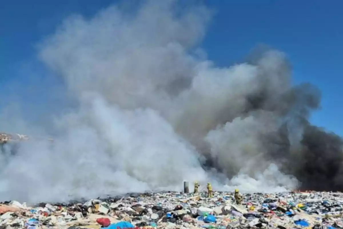 Incendio en un basurero con grandes columnas de humo y bomberos trabajando para controlar el fuego