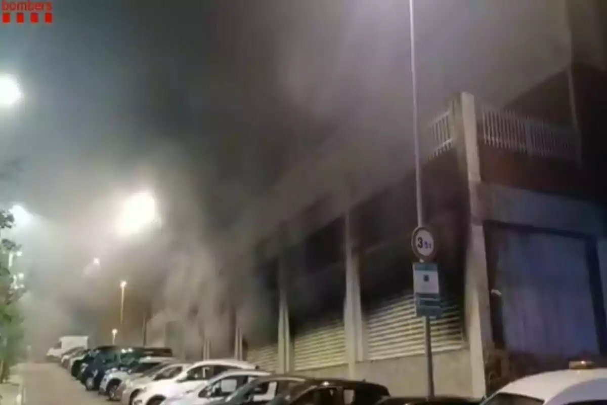 Varios coches estacionados junto a un edificio del que sale una gran cantidad de humo durante la noche