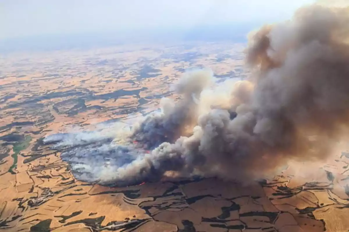 Vista aérea de un incendio forestal en una zona de campos agrícolas con una gran columna de humo elevándose sobre el paisaje.