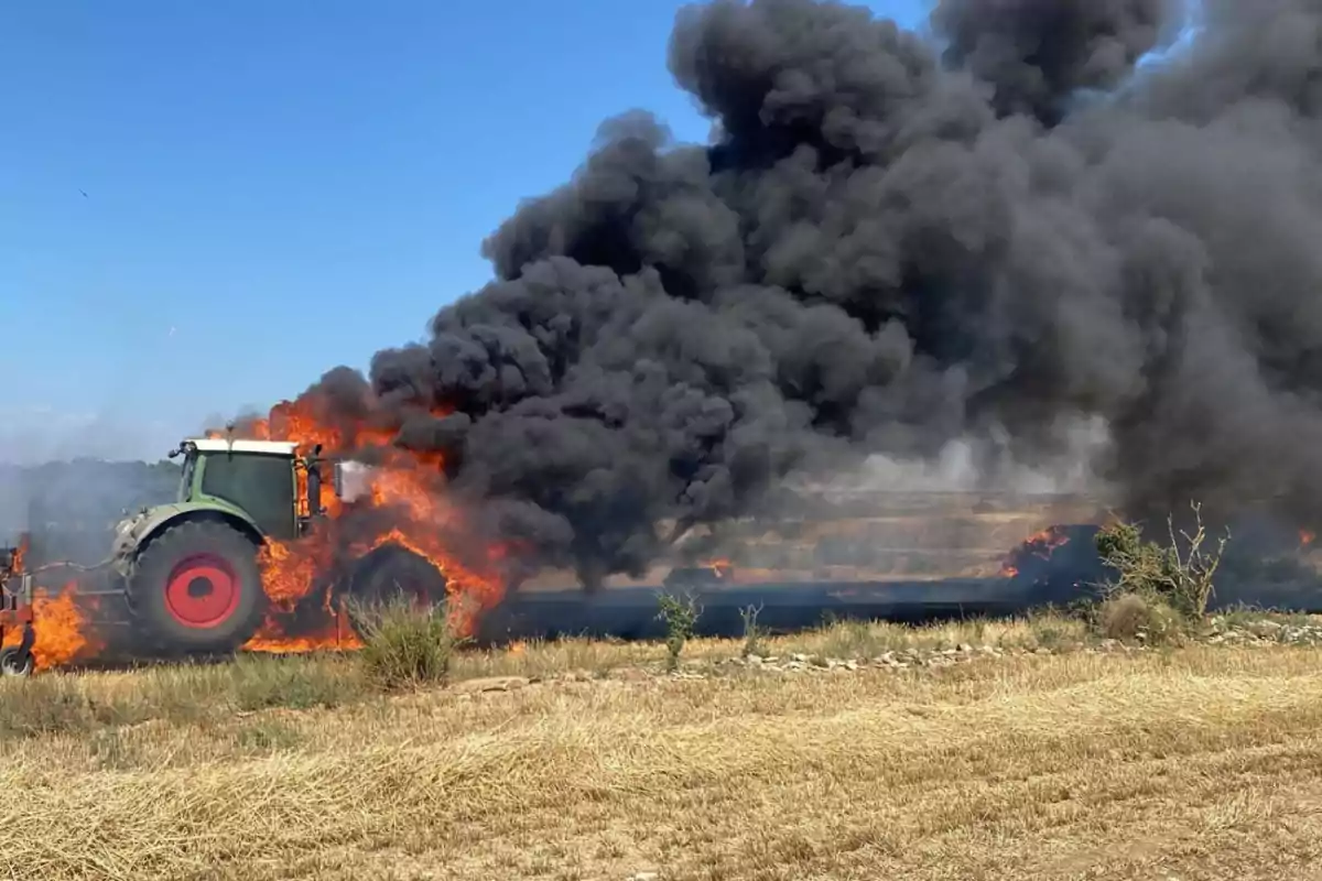 Tractor envoltat en flames en un camp amb una gran columna de fum negre que s’eleva cap al cel