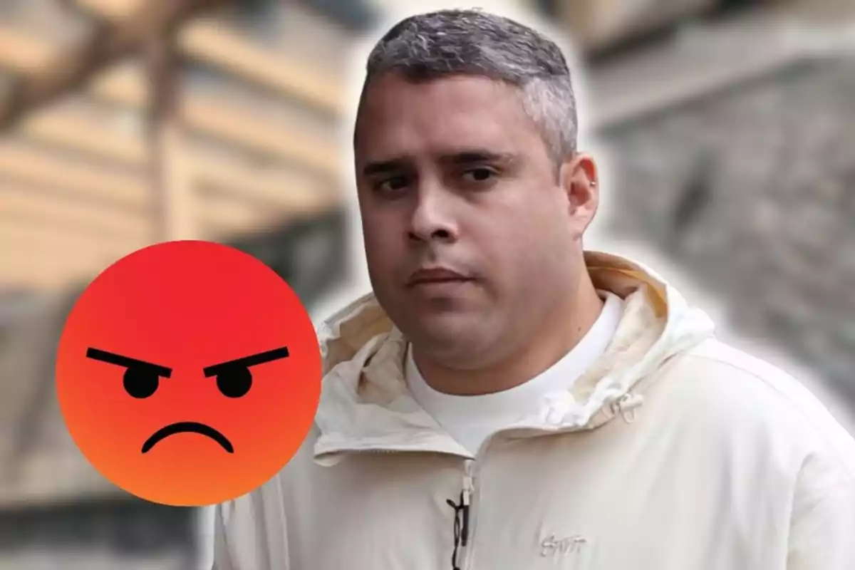 Home de cabell curt i canós amb expressió seriosa, portant una jaqueta clara, al costat d’un emoji d’enfadament sobre un fons urbà desenfocat