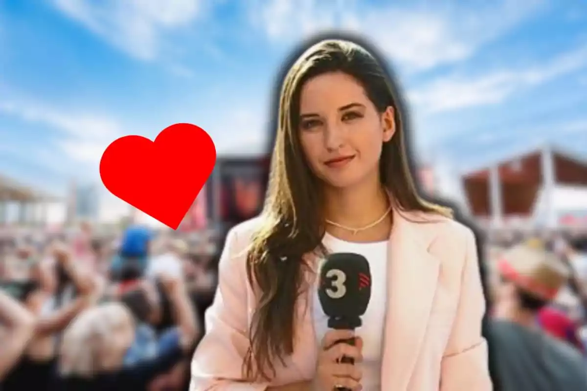 Jove reportera amb micròfon en un esdeveniment a l’aire lliure amb un gran cor vermell al seu costat i una multitud de fons