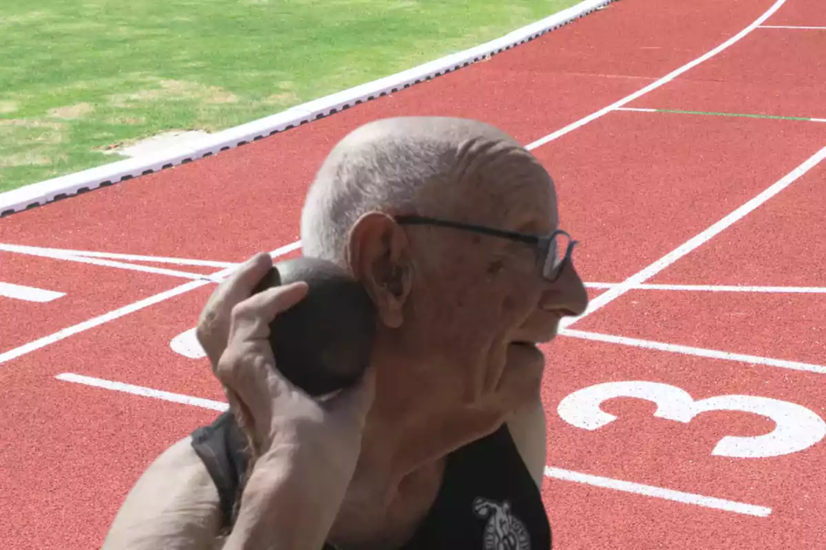 Hombre mayor con gafas preparándose para lanzar una bala en una pista de atletismo Hombre mayor con gafas preparándose para lanzar una bala en una pista de atletismo