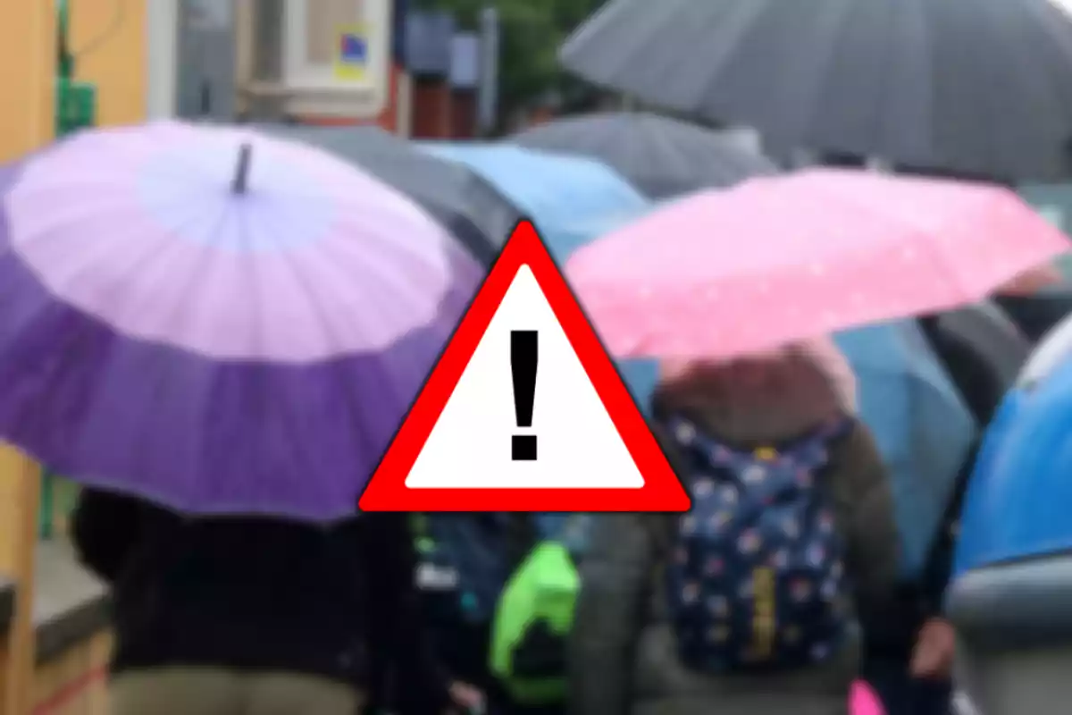 Persones amb paraigües de colors sota la pluja i un símbol d’advertència al centre Persones amb paraigües de colors sota la pluja i un símbol d’advertència al centre