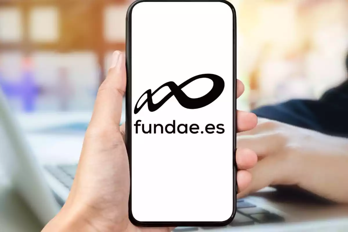 Persona sostenint un telèfon mòbil que mostra el logotip i la web fundae.es a la pantalla Persona sostenint un telèfon mòbil que mostra el logotip i la web fundae.es a la pantalla