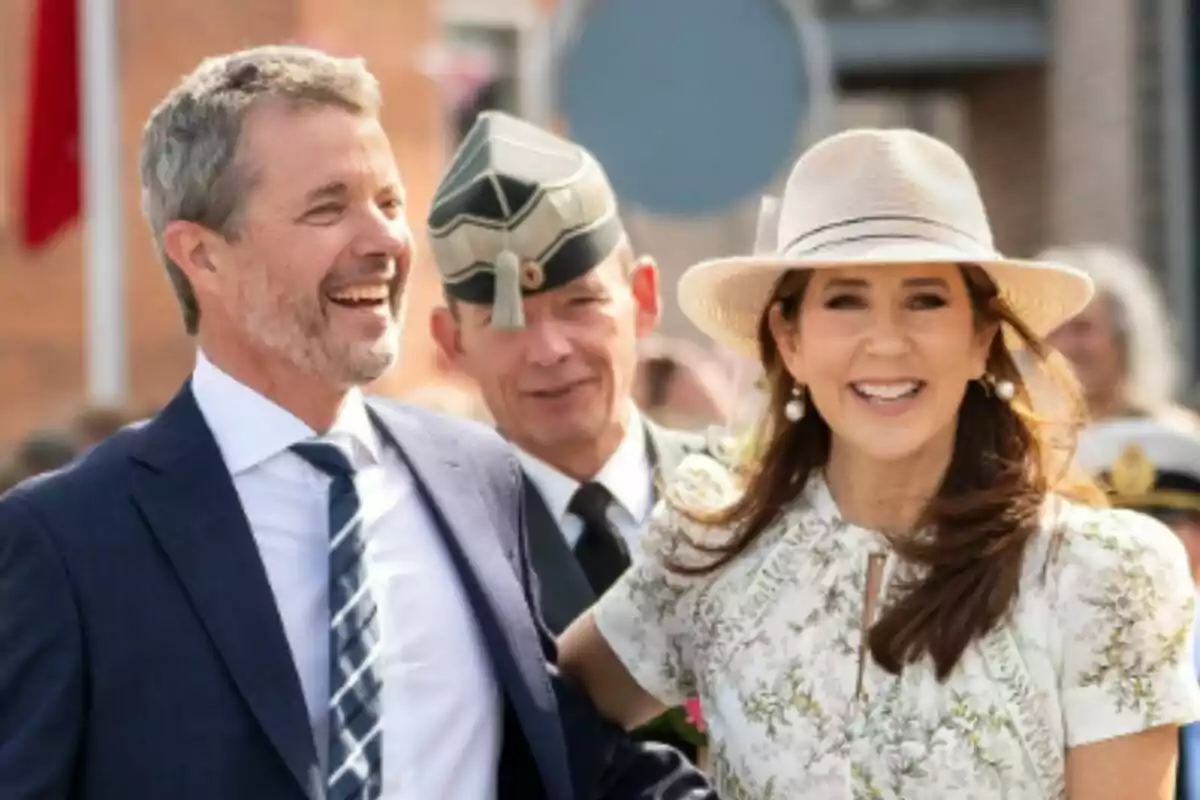 Smiling, elegantly dressed couple—Mary of Denmark and Frederik of Denmark—at an outdoor event accompanied by a man in military uniform. Smiling, elegantly dressed couple—Mary of Denmark and Frederik of Denmark—at an outdoor event accompanied by a man in military uniform.