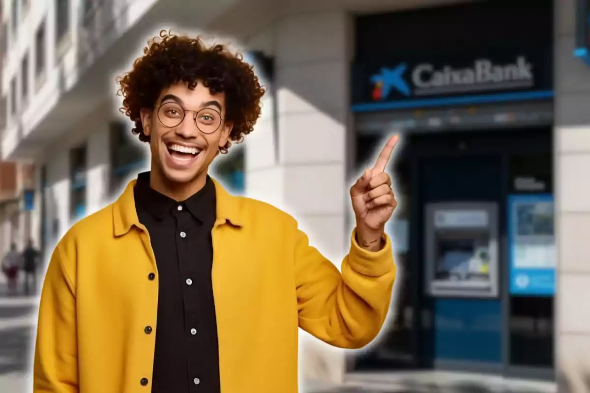 Jove somrient amb ulleres i jaqueta groga assenyalant cap a una sucursal de CaixaBank Jove somrient amb ulleres i jaqueta groga assenyalant cap a una sucursal de CaixaBank