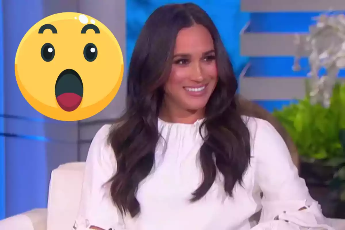 Dona de cabells llargs i foscos somriu asseguda en un sofà blanc amb un emoji de cara sorpresa gran al seu costat esquerre