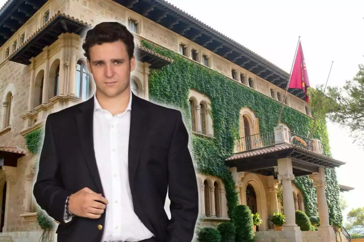 Joven con saco oscuro y camisa blanca posando frente a un edificio antiguo cubierto de enredaderas y con una bandera roja ondeando en la parte superior