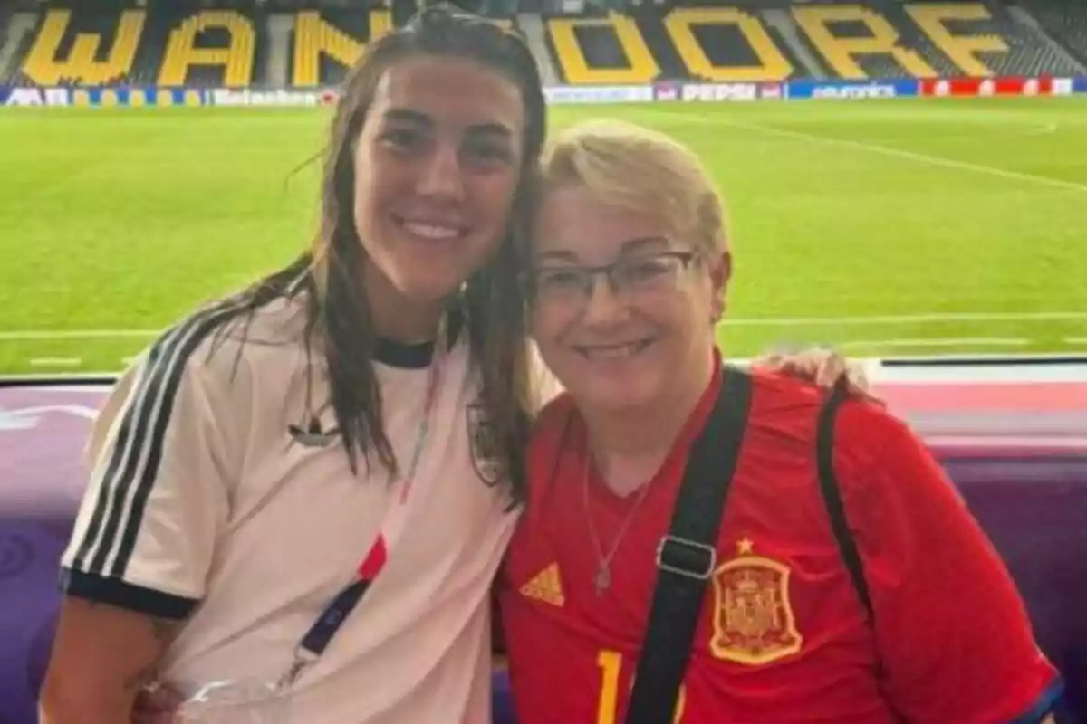 Dues dones somriuen abraçades en un estadi de futbol, una porta una samarreta blanca i l’altra una samarreta vermella de la selecció d’Espanya. Dues dones somriuen abraçades en un estadi de futbol, una porta una samarreta blanca i l’altra una samarreta vermella de la selecció d’Espanya.