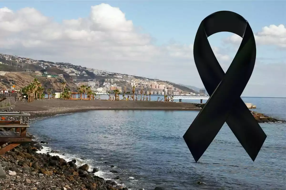 Platja de sorra fosca amb un llaç negre de dol en primer pla i muntanyes al fons