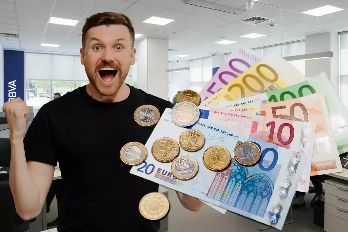 Hombre sonriente y emocionado sostiene billetes y monedas de euro en el interior de una oficina bancaria