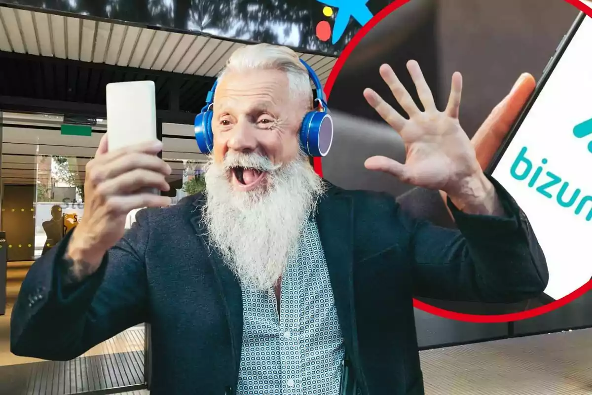 Hombre mayor con barba blanca usando audífonos azules y sonriendo mientras sostiene un teléfono móvil frente a una sucursal bancaria y un logo de Bizum en el fondo