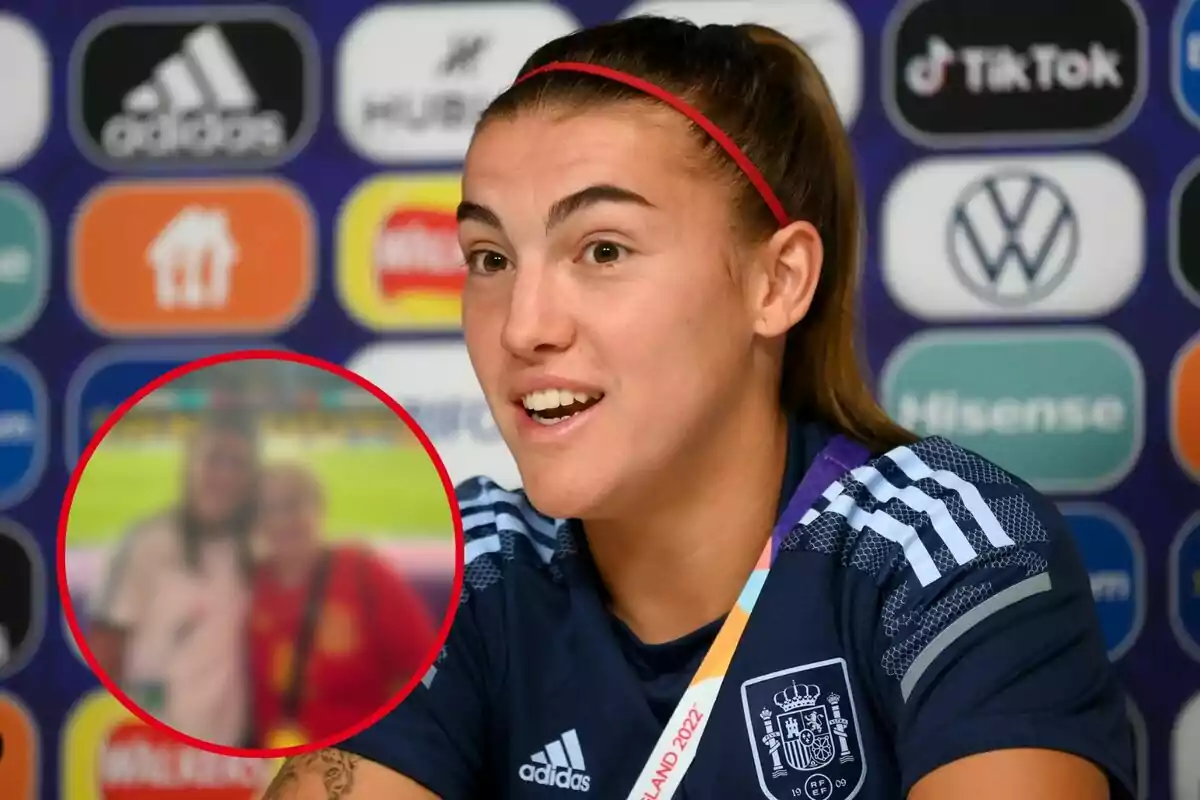Futbolista amb uniforme d’Espanya parlant en una roda de premsa amb un fons de logotips i un requadre que mostra una foto borrosa de dues persones en un estadi