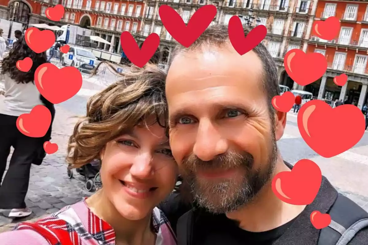 Parella somrient fent-se una selfie en una plaça amb cors vermells dibuixats al voltant de les seves cares