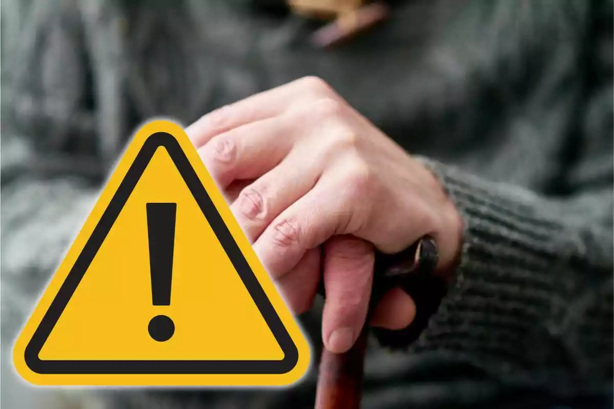 Mà d’una persona gran sostenint un bastó amb un símbol d’advertència groc superposat