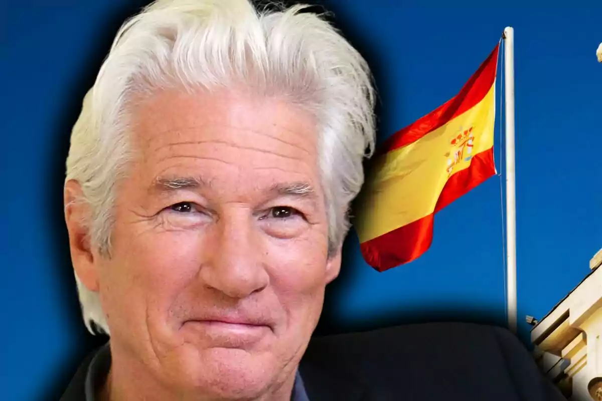Richard Gere smiling in the foreground with a Spanish flag waving in the background against a blue sky.