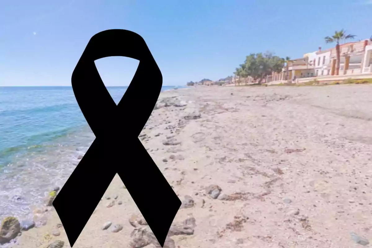 Playa con casas al fondo y un lazo negro de luto en el centro de la imagen