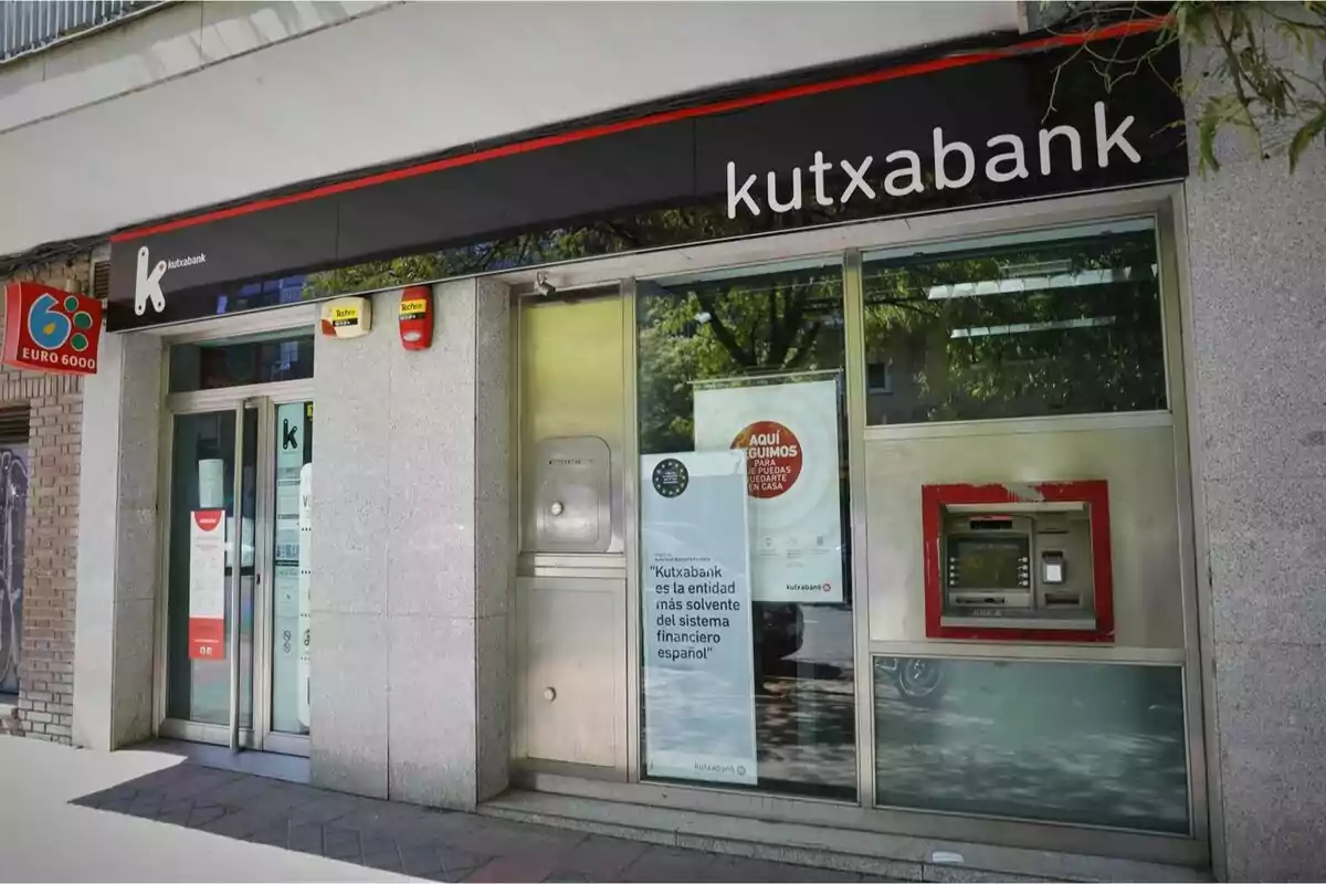 Façana d’una sucursal de Kutxabank amb un caixer automàtic i cartells informatius a la finestra Façana d’una sucursal de Kutxabank amb un caixer automàtic i cartells informatius a la finestra