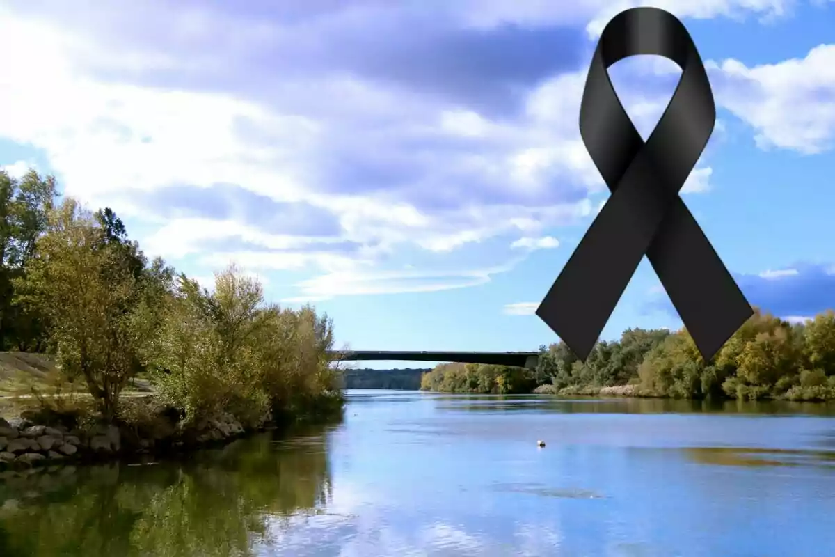 Paisatge de riu amb arbres i un pont al fons, cel parcialment ennuvolat i un llaç negre gran a la cantonada superior dreta