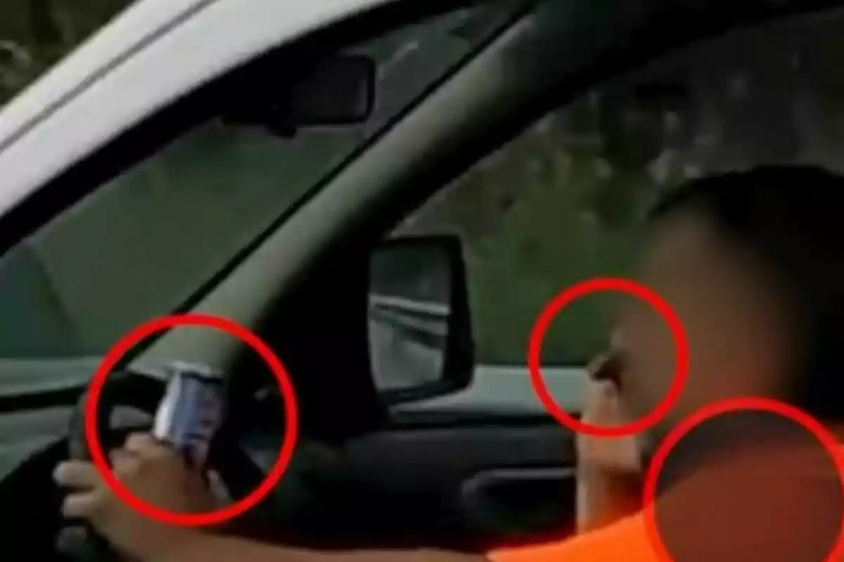 Persona conduint un automòbil mentre sosté una llauna amb una mà i es toca el nas amb l’altra, ambdues accions estan ressaltades amb cercles vermells.