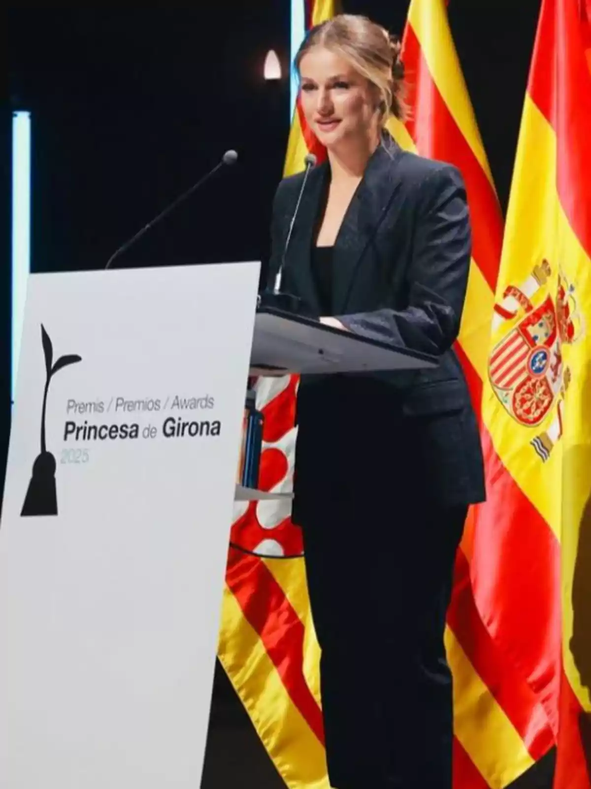 La princesa Leonor amb vestit fosc parlant en un faristol durant els Premis Princesa de Girona 2025 amb banderes d’Espanya i de Catalunya al fons La princesa Leonor amb vestit fosc parlant en un faristol durant els Premis Princesa de Girona 2025 amb banderes d’Espanya i de Catalunya al fons