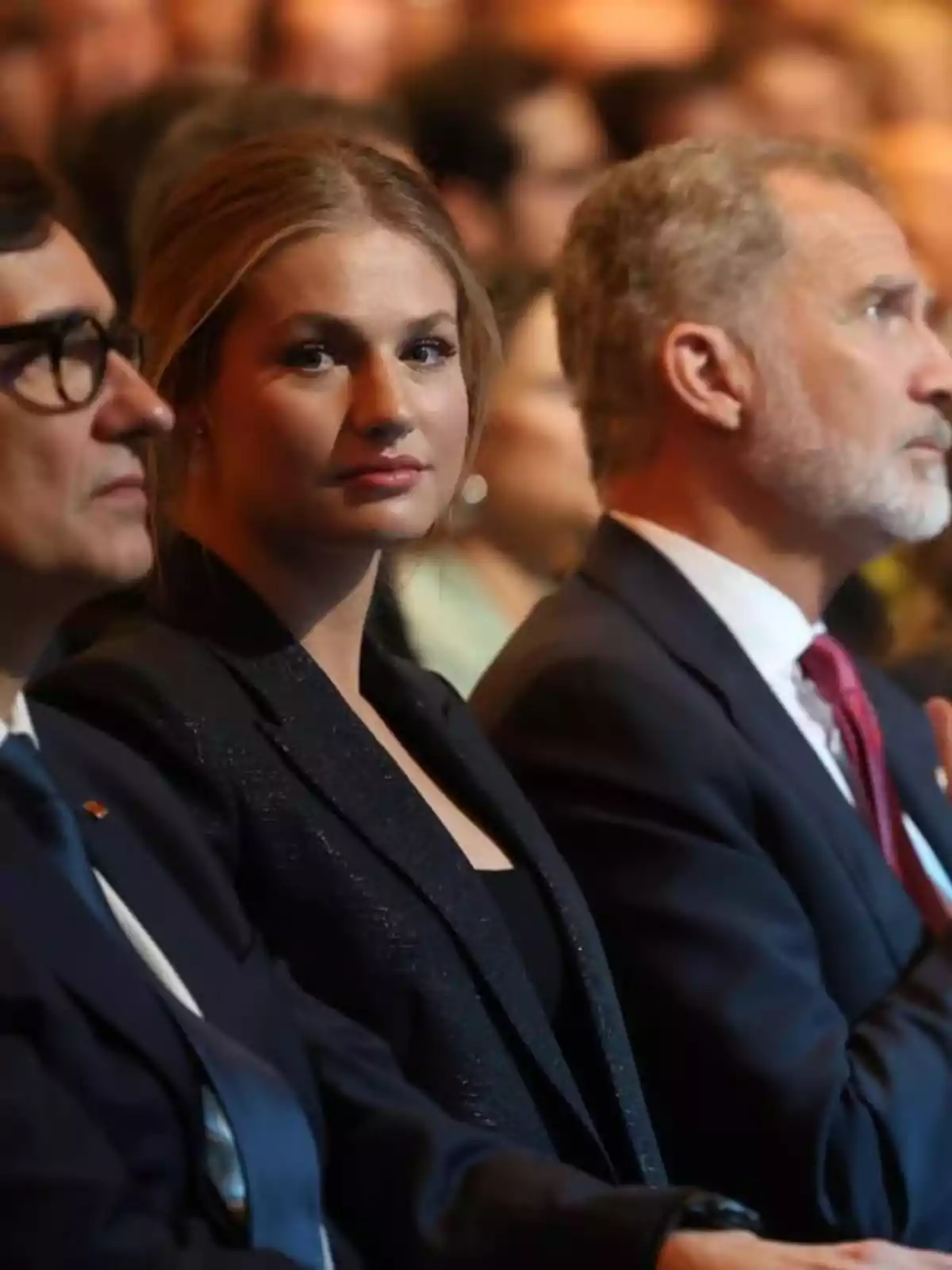 Salvador Illa, la princesa Leonor i Felip VI asseguts en un esdeveniment formal amb la dona al centre mirant cap a la càmera i els homes als costats mirant al front. Salvador Illa, la princesa Leonor i Felip VI asseguts en un esdeveniment formal amb la dona al centre mirant cap a la càmera i els homes als costats mirant al front.