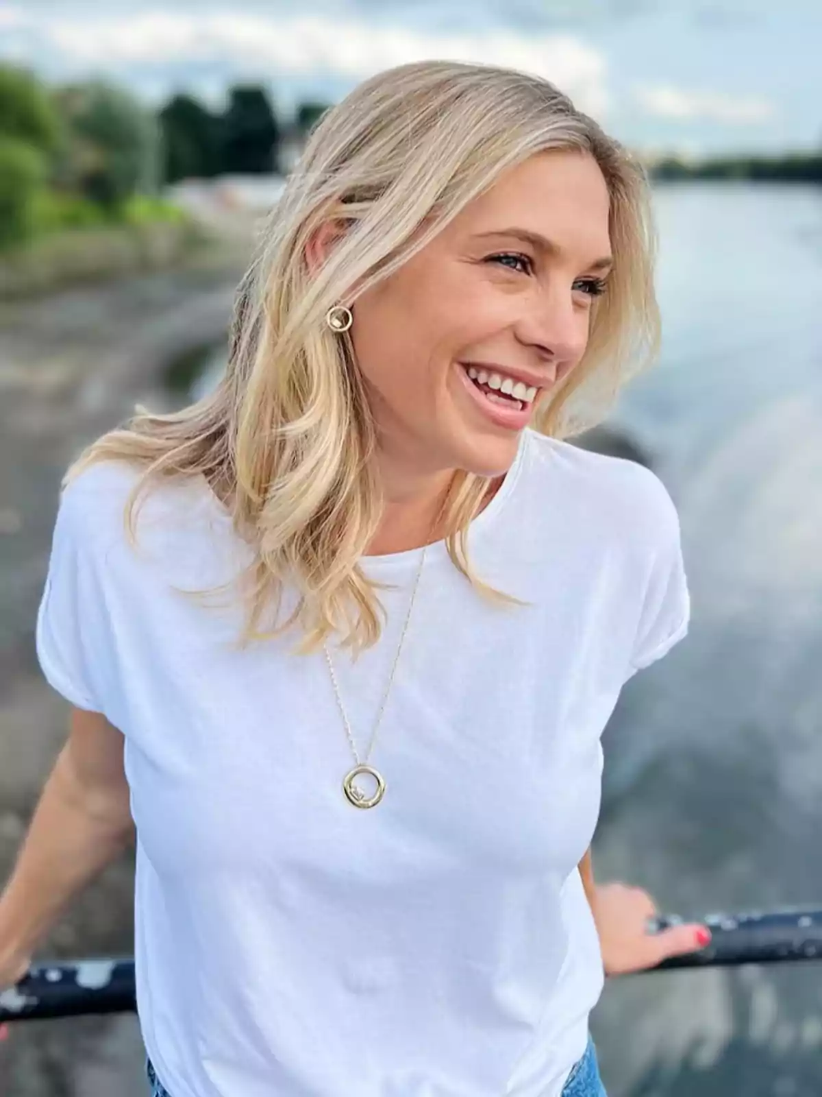 Chelsy Davy sonriente con camiseta blanca y collar dorado posando al aire libre junto a un cuerpo de agua Chelsy Davy sonriente con camiseta blanca y collar dorado posando al aire libre junto a un cuerpo de agua