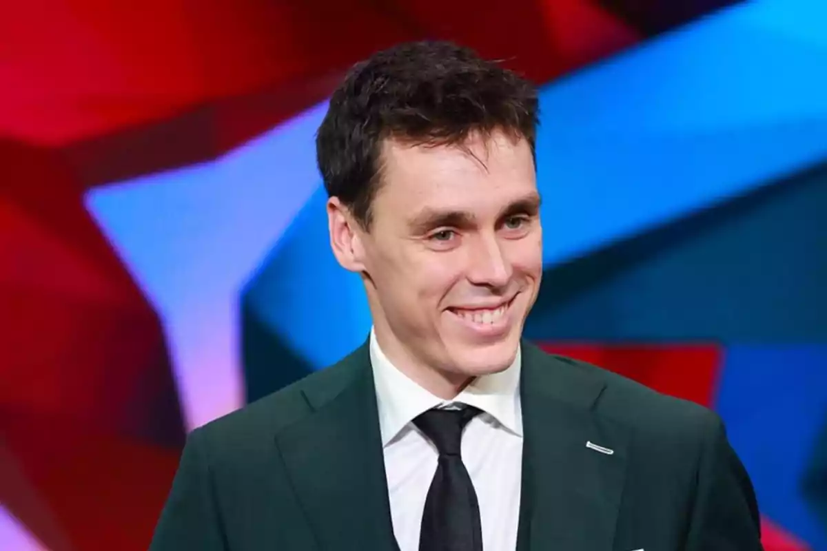 Príncep Louis Ducruet de cabell curt i fosc amb vestit verd fosc, camisa blanca i corbata negra, somrient davant d’un fons colorit desenfocat. Príncep Louis Ducruet de cabell curt i fosc amb vestit verd fosc, camisa blanca i corbata negra, somrient davant d’un fons colorit desenfocat.