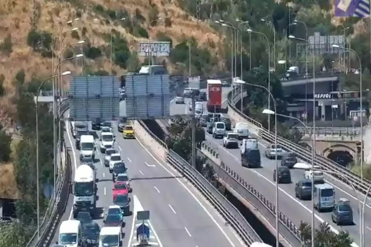 Tráfico denso en una autopista de varios carriles con vehículos circulando en ambas direcciones y una gasolinera al fondo