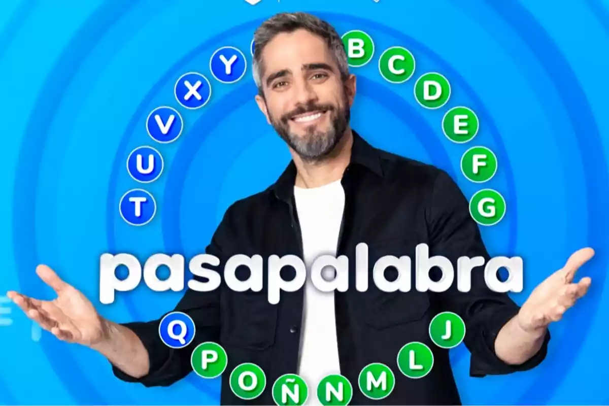 Home somrient amb barba i cabell curt davant d’un fons blau amb lletres en cercle i el text pasapalabra al centre Home somrient amb barba i cabell curt davant d’un fons blau amb lletres en cercle i el text pasapalabra al centre