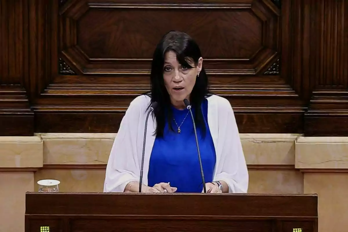 Dona de cabells foscos parlant en un faristol de fusta amb dos micròfons en un entorn institucional