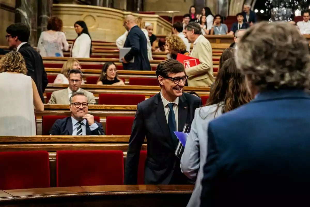 Persones conversant i somrient en un hemicicle amb seients vermells i ambient formal Persones conversant i somrient en un hemicicle amb seients vermells i ambient formal