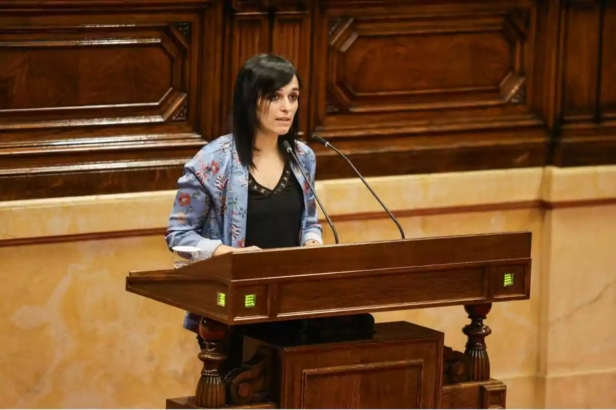 Dona de cabells foscos parlant en un faristol de fusta en un recinte parlamentari Dona de cabells foscos parlant en un faristol de fusta en un recinte parlamentari