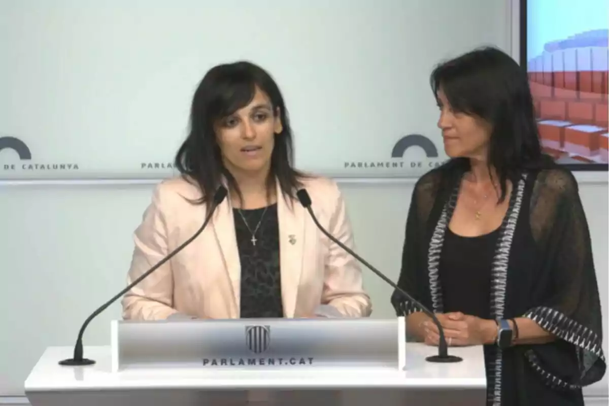 Dues dones estan dretes en un faristol del Parlament de Catalunya durant una roda de premsa.