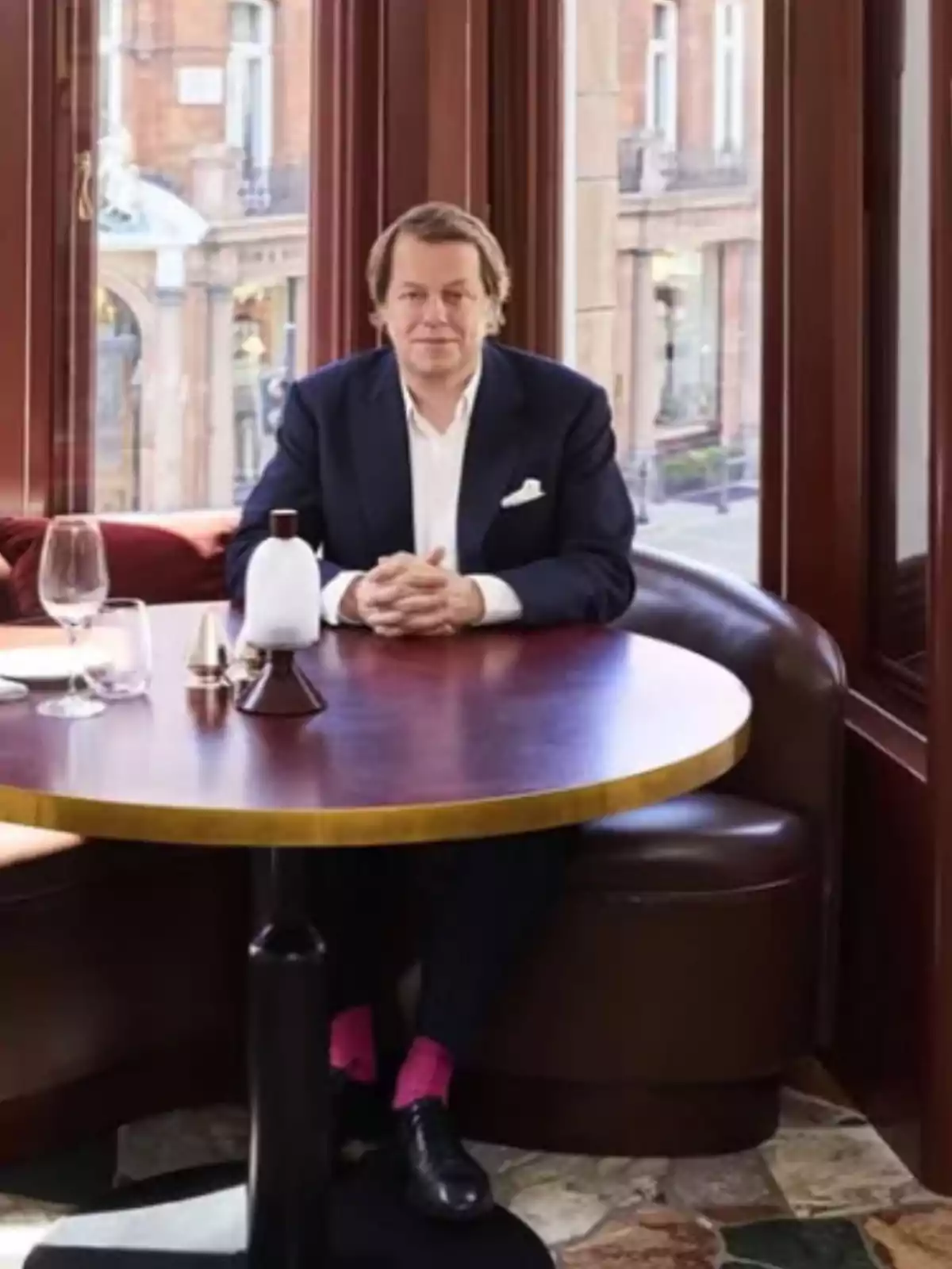 Man in a navy blue suit sitting alone at a round table in an upscale restaurant with large windows and natural light Man in a navy blue suit sitting alone at a round table in an upscale restaurant with large windows and natural light