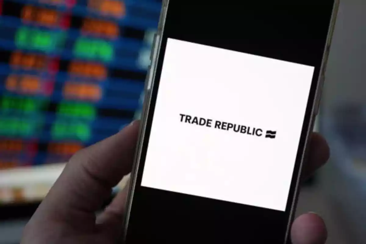 Persona sosteniendo un teléfono móvil que muestra el logo de Trade Republic en la pantalla, con un fondo borroso de gráficos de colores. Persona sosteniendo un teléfono móvil que muestra el logo de Trade Republic en la pantalla, con un fondo borroso de gráficos de colores.
