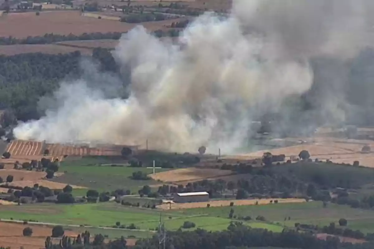Humo denso se eleva desde un campo agrícola en medio de una zona rural con vegetación y cultivos