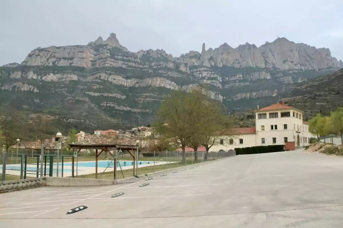 Estacionamiento vacío junto a una piscina y un edificio blanco con montañas rocosas al fondo Estacionamiento vacío junto a una piscina y un edificio blanco con montañas rocosas al fondo